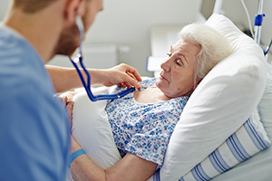 Caregiver using stethoscope on elderly woman in bed